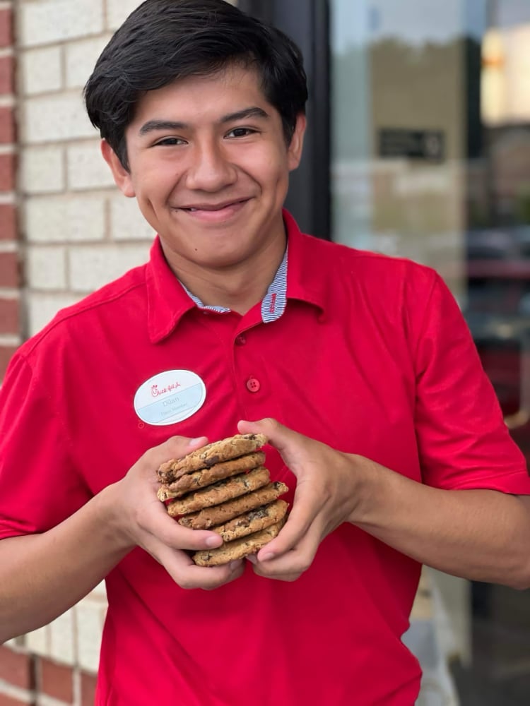Smiling Chick-fil-A team member holding a stack of Chocolate Chunk Cookies
